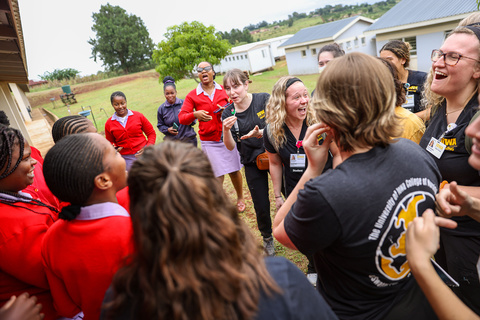 A group of laughing students, some in black Iowa scrubs and som in red cardigans, laugh and talk outside. 