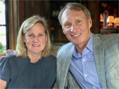 Portrait of Andy and Susie Code sitting together, fireplace in background. 